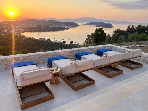 a group of lounge chairs on a patio with the sunset at Villa Hillside Skiathos in Skiathos