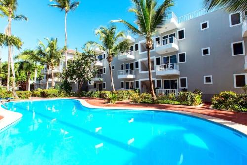 a swimming pool in front of a building with palm trees at MIRABELLA SOL CARIBE SUITES playa LOS CORALES in Punta Cana