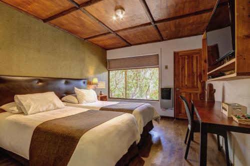 a hotel room with two beds and a desk and a window at Hoteles Pueblo de Tierra in San Pedro de Atacama