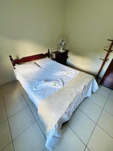a bedroom with a bed with white sheets and a fan at Casa do Carol Sana in Macaé