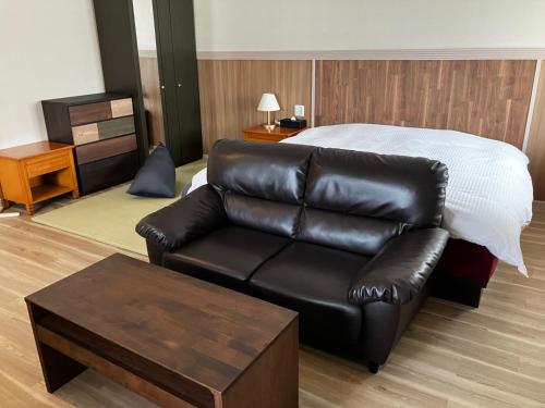 a living room with a bed and a leather couch at セントロ大隅ホテルオオサキ in Kanoya