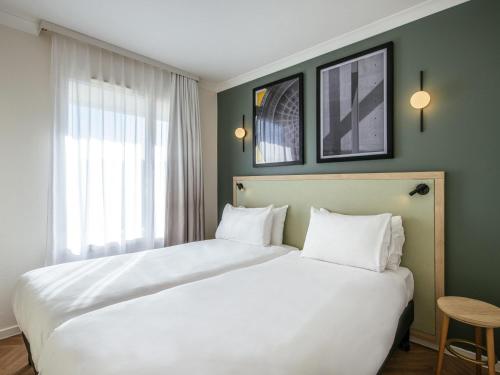 a bedroom with a large white bed and a window at Aparthotel Adagio Paris Buttes Chaumont in Paris