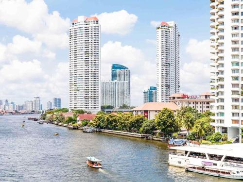 a river with boats in a city with tall buildings at Ibis Bangkok Riverside in Bangkok