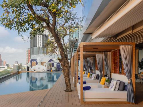 a hotel pool with lounge chairs and a tree at Novotel Bangkok Platinum Pratunam in Bangkok