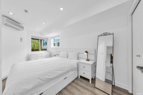 a white bedroom with a large bed and a mirror at Central Alpine Condo in Whistler