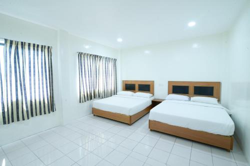 two beds in a white room with two windows at Mersing Hotel in Mersing