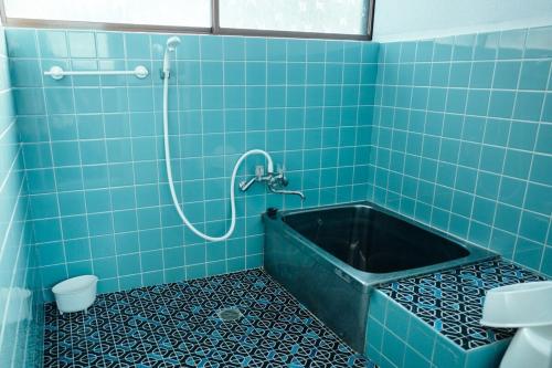 a blue tiled bathroom with a tub with a shower at Kumano Base in Tanabe