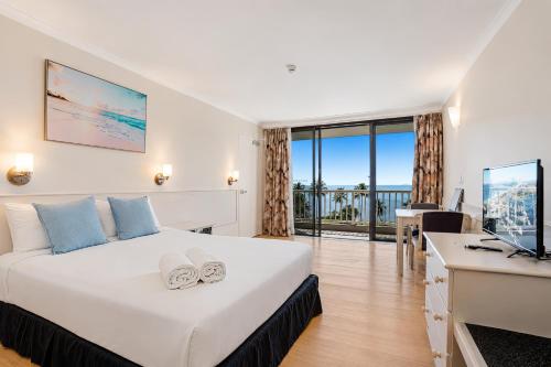 ein Hotelzimmer mit Bett, Schreibtisch und Fernseher in der Unterkunft The Oceanfront in Cairns