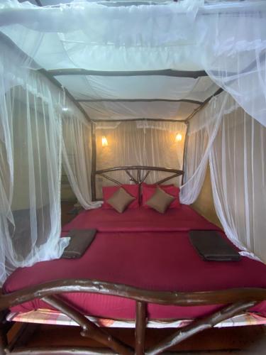 a bedroom with a canopy bed with red sheets and pillows at The Nirwana cottage in Ella