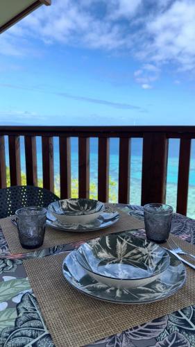 a table with plates and bowls on a balcony with the ocean at Bungalow Omati in Tahateao