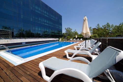 - Piscina con tumbonas blancas y sombrilla en Abba Playa Gijón, en Gijón