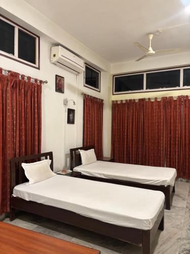 two beds in a room with red curtains at Hotel Nikita in Jorhat