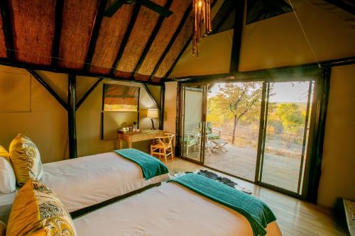 a bedroom with two beds in a room with a balcony at Masuwe Lodge in Victoria Falls