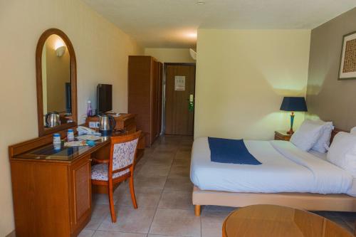 ein Hotelzimmer mit einem Bett und einem Schreibtisch und einem Bett und einem Tisch in der Unterkunft Hôtel Elaïs in Pointe-Noire
