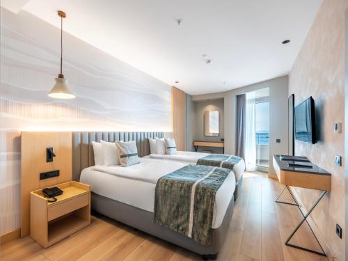 a hotel room with a large bed and a television at Korumar Hotel Deluxe in Kuşadası