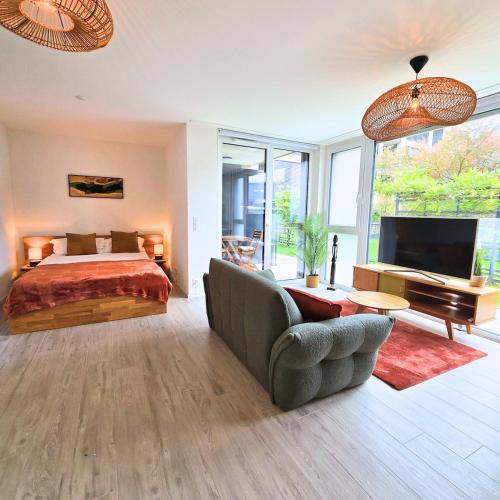 a bedroom with a bed and a couch and a television at Studio Premium - Jardin privatif - Parking in Epalinges