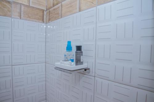 a white tiled bathroom with a bottle of water on a shelf at Andrew View Hotel in Dar es Salaam