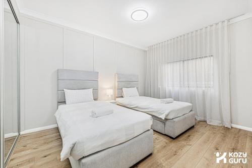 two beds in a bedroom with white walls and wood floors at KozyGuru | Penrith | Spacious Ground Floor Gem in Penrith