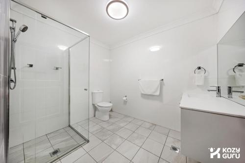a white bathroom with a shower and a toilet at KozyGuru | Penrith | Spacious Ground Floor Gem in Penrith