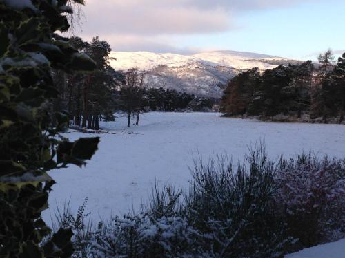 a field covered in snow with mountains in the background at Camusmore House in Aviemore