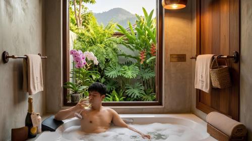 a man in a bath tub with a glass of wine at Wellness Resort Rayong Managed by the SCN in Ban Huai Pla Kang