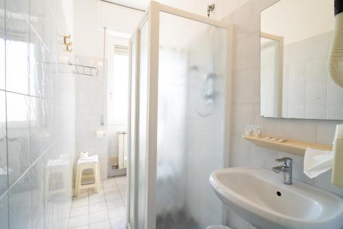 a white bathroom with a shower and a sink at Hotel Corallo in Pietra Ligure