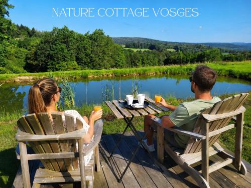 a man and woman sitting at a picnic table by a lake at Nature Cottage Vosges in Anould