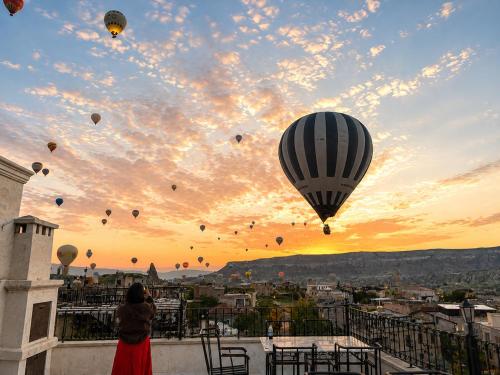 a woman standing on a balcony looking at hot air balloons at Milat Cave in Göreme