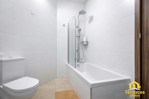 a white bathroom with a toilet and a bath tub at The Terraces Seafront Getaway Malta 3 Bedroom Apartment in St. Paul's Bay