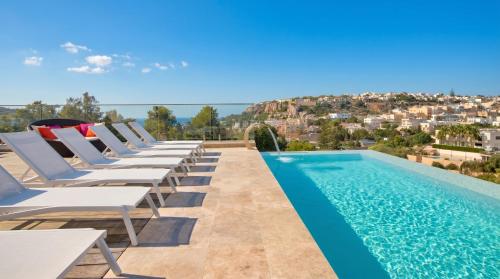 a row of lounge chairs next to a swimming pool at Maltese Luxury Villas - Sunset Infinity Pools, Indoor Heated Pools and More! in Mellieħa