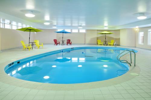 una piscina en una habitación grande con sillas y sombrillas en Greenwood Inn & Suites en Corner Brook