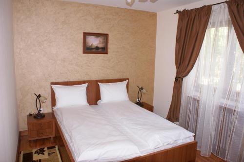 a bedroom with a bed with white sheets and a window at Pensiunea Normandia in Timişoara