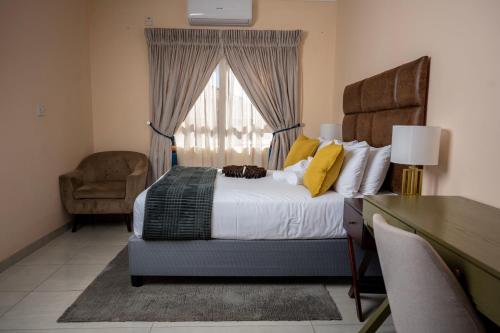 a bedroom with a bed and a chair and a window at Sycamon Suites in Jwaneng