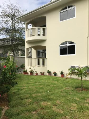 a white house with a porch and a yard at Flower Garden Self-Catering Apartments in Beau Vallon