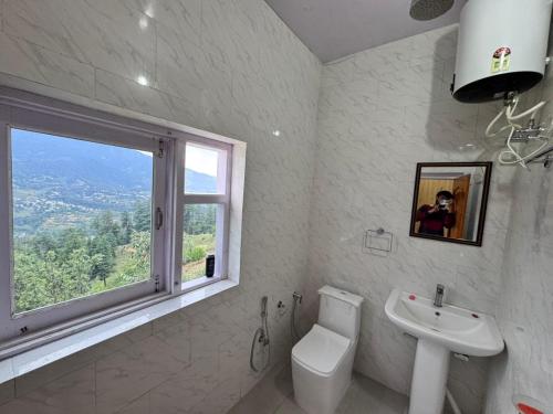 a bathroom with a toilet and a sink and a window at Seraahi Hills Resort in Bhadarwāh