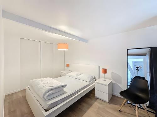 a white bedroom with a white bed and a black chair at Gite Donald proche Colmar in Ingersheim