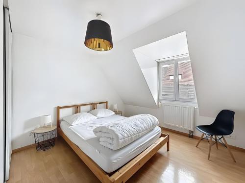 a white bedroom with a bed and a black chair at Gite Marie proche Colmar in Ingersheim