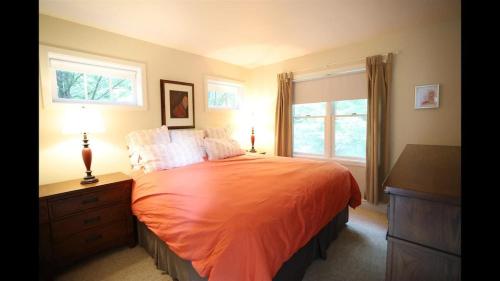 a bedroom with a bed with an orange bedspread and two windows at Weetamoo Trail 50 Estates Relax in the White Mountains in Campton