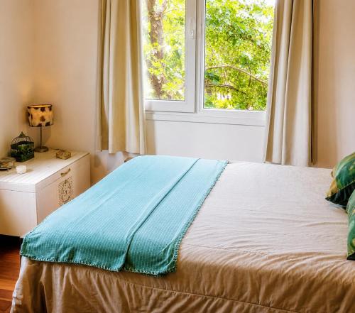 a bed with a blue blanket on it in front of a window at Casa Verde in La Cumbre