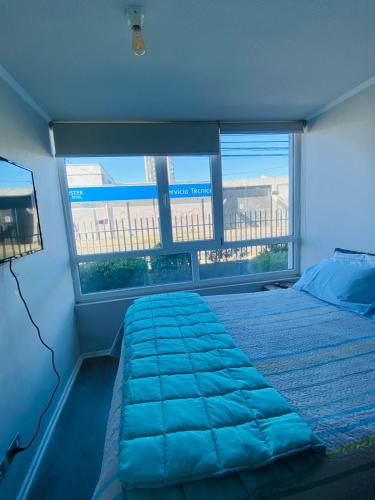 a bedroom with a bed with blue sheets and two windows at Acogedor Apartamento 2D1B Edificio Aldunate in Temuco