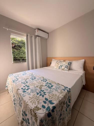 a bedroom with a bed with a flowered blanket and a window at Season Ilhéus in Ilhéus