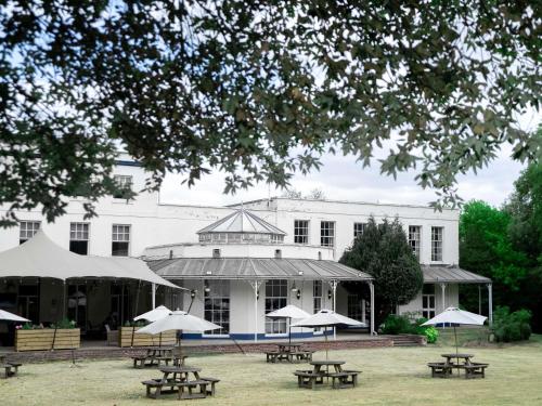 a building with tables and umbrellas in front of it at Mercure Thurrock Stifford Hall in Grays Thurrock