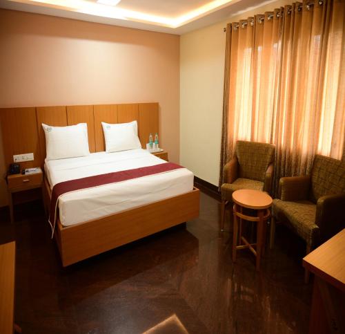 a hotel room with a bed and two chairs at Hotel PAMS in Mayiladuthurai