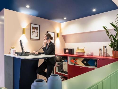 a woman sitting at a desk talking on a cell phone at Aparthotel Adagio Paris Haussmann Champs Elysées in Paris