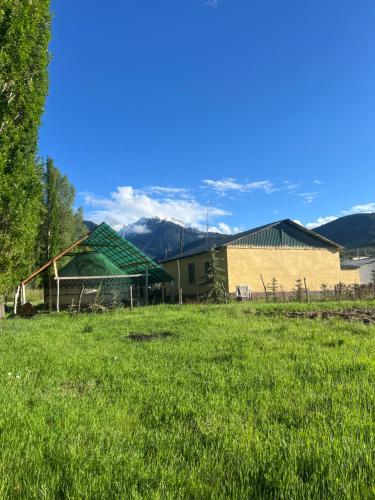 a field of grass with a house and mountains in the background at Ak-Suu Eco House in Teploklyuchinskoye