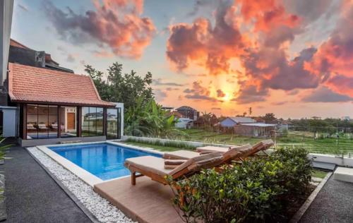 a pool with chairs and a house with a sunset at Emy Kerobokan in Kerobokan