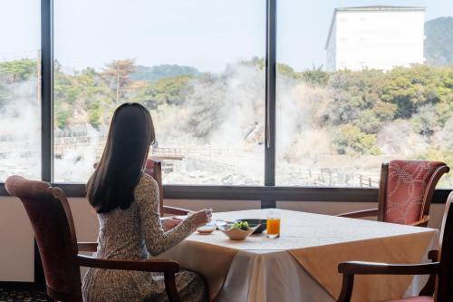 Eine Frau sitzt in einem Restaurant an einem Tisch und schaut aus dem Fenster. in der Unterkunft Unzen Kyushu Hotel in Unzen
