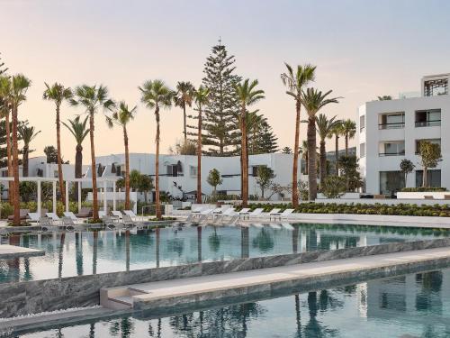a swimming pool with palm trees and white buildings at Creta Palace, A Resort to Live in Rethymno