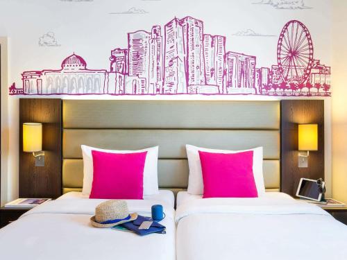 two beds in a hotel room with a mural of a city at ibis Styles Sharjah in Sharjah