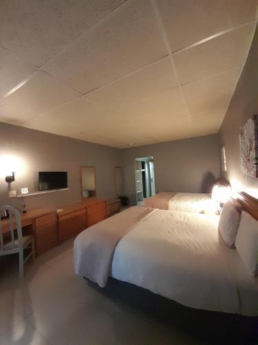 a bedroom with two beds and a desk and a television at Matsapha Hotel in Mahlanya